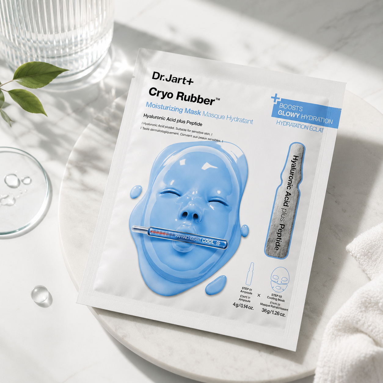 Dr.Jart+ Cryo Rubber Moisturizing Mask with Hyaluronic Acid Plus Peptide sachet elegantly displayed on a white marble tray beside glass skincare accessories, water droplets, soft towels and fresh greenery, creating a clean spa-inspired atmosphere that emphasizes deep hydration, soothing care and a refreshing cooling skincare experience.
