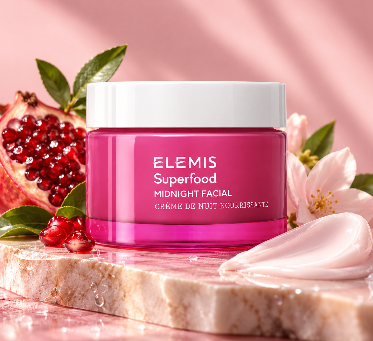 ELEMIS Superfood Midnight Facial nourishing overnight face cream in a vibrant pink jar with a white lid, elegantly displayed alongside fresh pomegranate, delicate pink flowers and creamy skincare texture. A luxurious hydrating night cream designed to nourish, soften and replenish skin overnight.