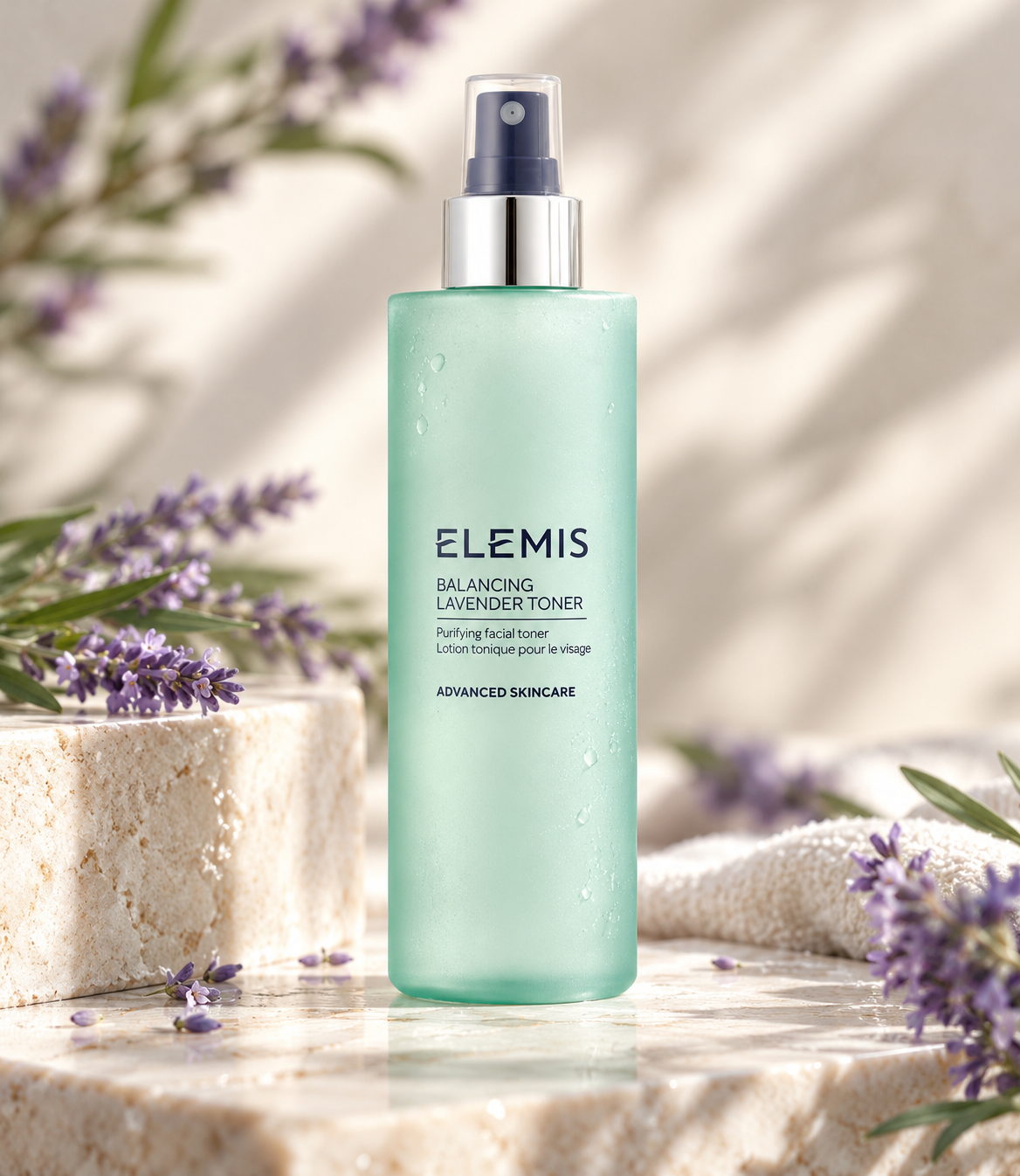 ELEMIS Balancing Lavender Toner purifying facial toner in an elegant mint-green spray bottle with a silver pump, displayed on natural stone surrounded by fresh lavender flowers and soft towels. A refreshing skincare toner designed to balance, purify and tone the skin.
